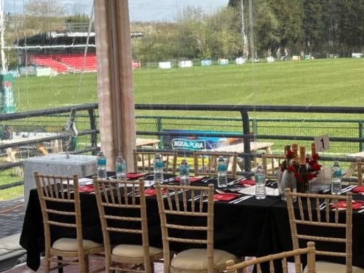 A long table dressed in black linen beside the clear marquee wall, with a stand beyond