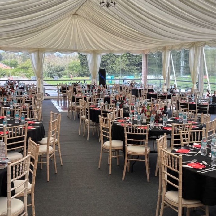 An aisle between dressed round tables and chiavari chairs, under a pleated marquee ceiling with a chandelier
